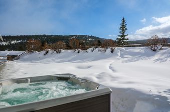 A bubbling hot tub surrounded by snow and pine trees at Southfork Retreat.