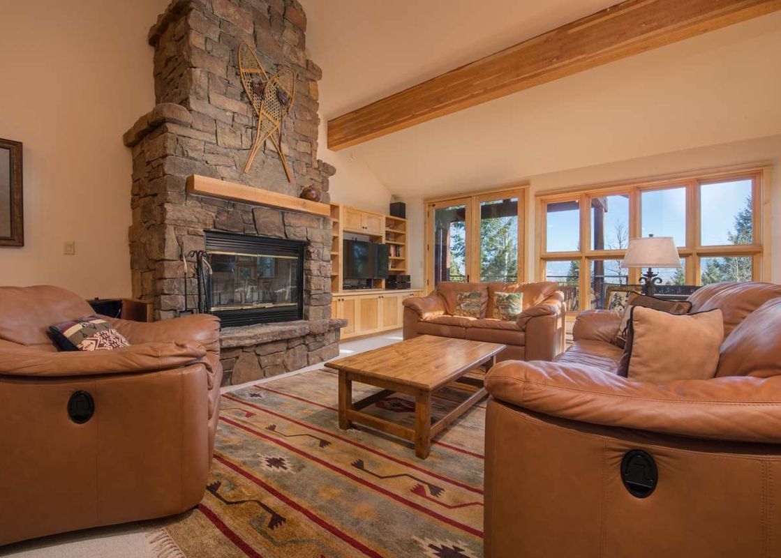 Cozy living room in Moose Creek 33 with a towering stone fireplace, leather sofas, and large windows.
