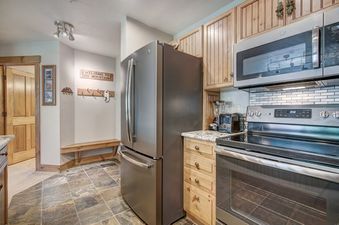 A modern kitchen and entryway inside the Mountain Thunder Lodge 1 Bedroom featuring stainless steel appliances and slate tile floors.