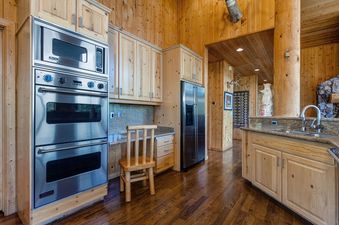 A spacious kitchen with rustic wood finishes, stainless steel appliances, and a granite countertop island with a sink.