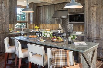 A rustic-chic kitchen with reclaimed wood cabinetry, a granite island with bar stools, stainless steel appliances, and a window offering an exterior view.