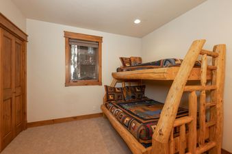 The bunk bedroom at the Lodge at Cucumber Patch is outfitted with sturdy wooden bunk beds, featuring rustic bedding in earthy tones and a window that offers a glimpse of the surrounding nature.
