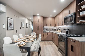 A modern kitchen and dining area with light wood cabinetry, a black dining table, and white chairs.