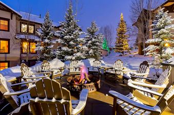 The outdoor common area at EagleRidge Townhomes 1479 is illuminated at dusk, showcasing a circular fire pit surrounded by Adirondack chairs, all covered in fresh snow.
