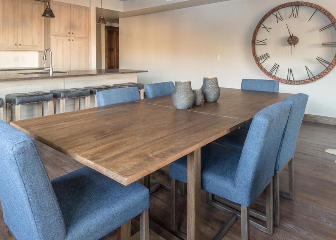 A spacious dining area with a wooden table, blue chairs, and an adjacent kitchen with light wood cabinets and a large island in Mountain Lake Condo 401B.