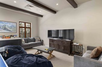 A game room with a grey couch, a coffee table with two coasters on it, a large TV, a game shelf with board games, and a ping pong table.