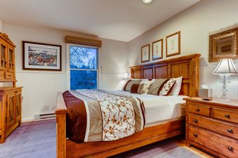 A cozy bedroom with a large wooden bed, light-colored walls, and a window with a view of trees outside.