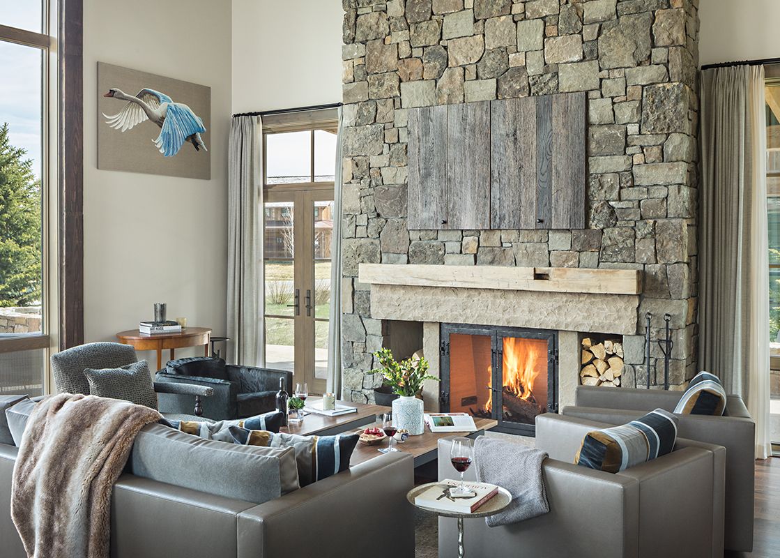 A rustic-chic living room at Fish Creek Lodge 63 featuring a large stone fireplace, plush leather sofas, and expansive windows offering scenic views of the outdoors.