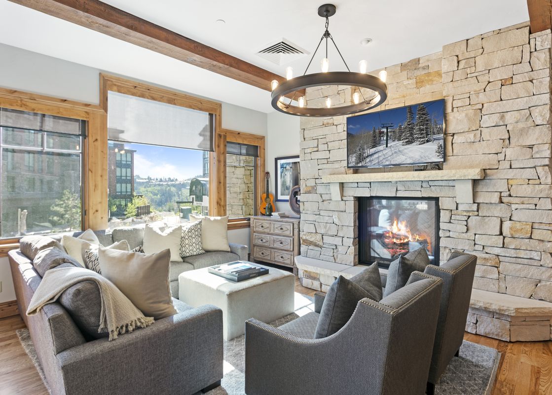 A cozy and bright living room at Silver Strike Lodge 302 features plush seating, a stone fireplace with a TV above, and large windows offering scenic views.