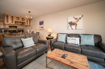 The living area of Silverado I C101, featuring two comfortable sofas and a rustic coffee table, opens to the fully equipped kitchen and dining space.