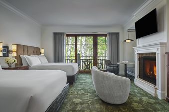 A hotel room with two queen beds, a fireplace, and a balcony with a view of trees.