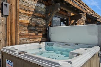 A sparkling hot tub with clear water, set against a rustic wooden building exterior under a bright blue sky.