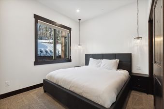 A cozy bedroom at Last Chair Lair featuring a king-sized bed, stylish pendant lights, and a window with a snowy outdoor view.