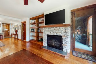 A cozy lounge area in BlueSky Breckenridge 205 features a stone fireplace, a wall-mounted TV, built-in wooden shelves, and an exterior glass door.