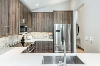 A modern kitchen with wood cabinets, stainless steel appliances, and white countertops.