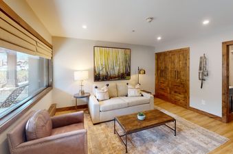 A living room with a couch, two chairs, a coffee table, a painting, a large window, and a door leading to a bathroom.