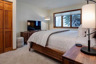 A cozy bedroom at Ranch at Steamboat RA203 with a large wooden bed, flat-screen TV, and a window overlooking snow-covered trees.