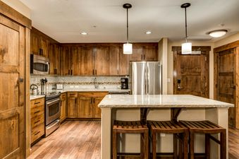 The kitchen at Trailhead Lodge 2105 features warm wooden cabinetry, stainless steel appliances, granite countertops, and an island with bar stools.