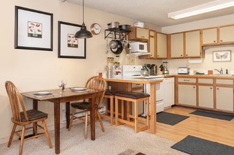 The image shows the kitchen and dining area of Snowblaze E102, featuring wooden furniture, cream-colored cabinets, and modern appliances.