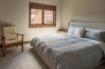A cozy bedroom with a comfortable bed, a wooden chair, and a window offering a glimpse of the outdoors.