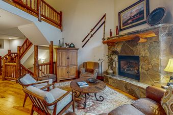 Cozy living room with a fireplace, a wood-burning stove, comfortable seating, and a large window with views of the mountains.