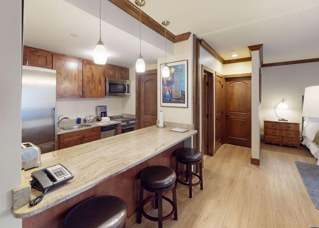 A kitchen with a small breakfast bar, bar stools, and stainless steel appliances.