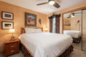 The king-sized bedroom at Snow Flower 124 Park City features a comfortable bed with white linens, rustic wooden nightstands, and Southwestern-themed decor including a ceiling fan and framed artwork.