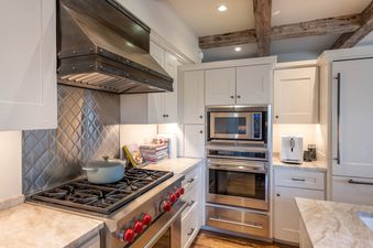 A modern kitchen with stainless steel appliances, white cabinets, and rustic wood ceiling beams in Shooting Star Cabin 05.