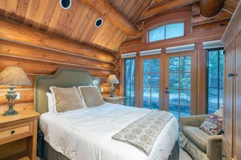 A rustic bedroom in Summit Cabin See Forever Cabin 103 with log walls, a vaulted ceiling, a plush bed, and large windows looking out onto a wooded landscape.