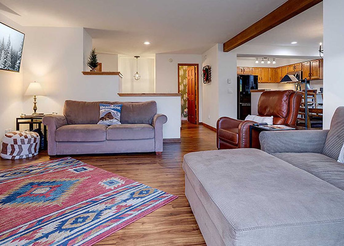 An expansive living area in Ranch at Steamboat RA517, featuring a comfortable sofa, a vibrant area rug, and an adjoining kitchen with wooden cabinetry.