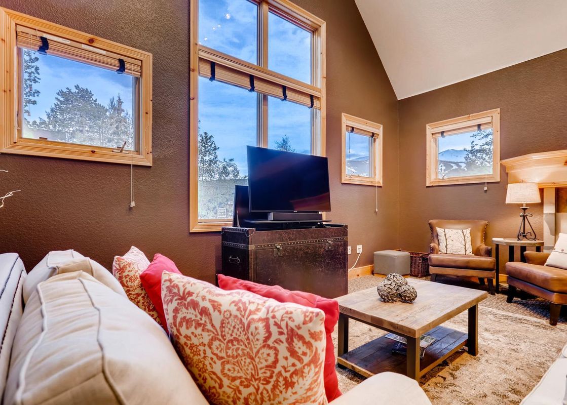 A cozy living room at the Ridge Street Cottage with plush seating, a large television, and stunning mountain views from multiple windows.