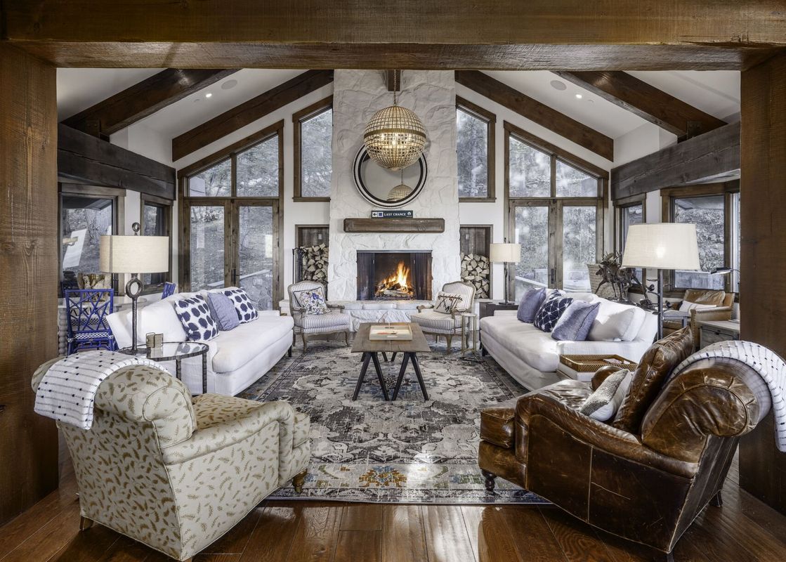 A luxurious great room at Silver Lake Slopeside features a grand stone fireplace, vaulted wooden beam ceilings, and large windows with winter views, furnished with plush sofas and elegant armchairs.