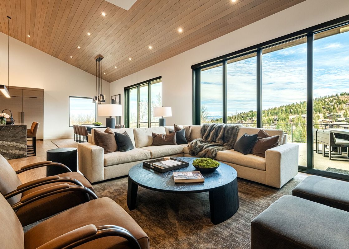 A modern living area at Deer Valley Luxe at Moonshadow with a large sectional, leather armchairs, and floor-to-ceiling windows showing mountain views.