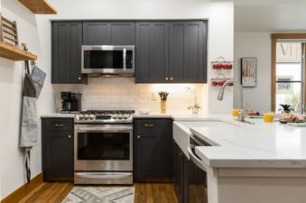 The kitchen at 118 Villa Montane features elegant dark cabinetry, stainless steel appliances, and bright white countertops, with a large window offering an exterior view.