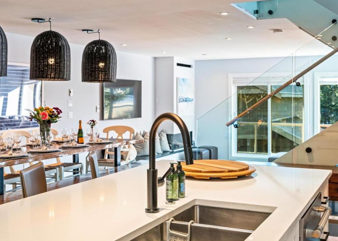 The open-concept kitchen and dining area at St Moritz Townhomes features a large kitchen island, a set dining table, and a contemporary glass and wood staircase, creating a luxurious and inviting living space.