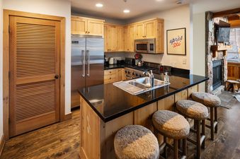 A modern kitchen at Portico Pines featuring wooden cabinets, black countertops, stainless steel appliances, and a kitchen island with four barstools.