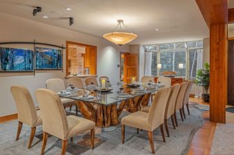 A dining room with a large wooden table, a glass top and a chandelier above