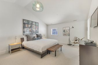 A bright and spacious bedroom at Stillson Meadow features a large bed, modern lamps, unique artwork, and a cowhide chair, creating a comfortable and stylish retreat.