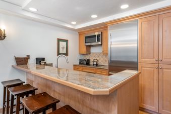 The kitchen counter features a granite countertop, a sink with a modern faucet, and a small coffee maker on the left, with bar stools in the foreground.