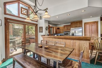 A wooden dining table with chairs and a bench sit in front of a sliding glass door that leads to a patio.