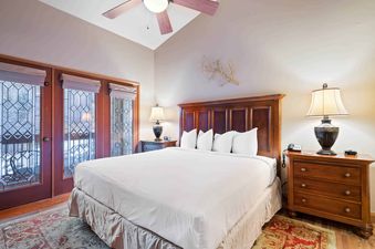 A master bedroom at The Charter B4305 featuring a king-sized bed, wooden nightstands with lamps, and glass doors with an exterior view.