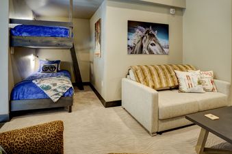 A cozy living room with a bunk bed in the corner, a couch with fur throw pillows, and a small coffee table.