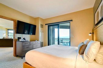 The Grand Summit Lodge Studio Residence features a comfortable bedroom with a large bed, a TV, and a balcony offering scenic views.