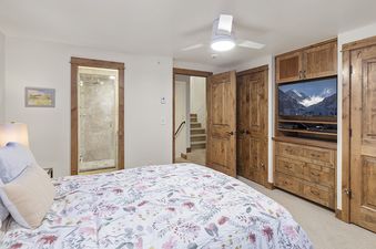 A bedroom with a queen size bed, nightstand, lamp, and a large TV.