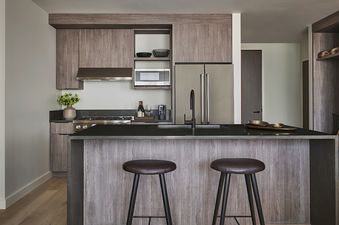 The kitchen in Pendry Two Bedroom Resort King Residences features a black granite countertop, stainless steel appliances, and a large island with two bar stools.