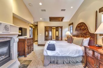 A luxurious bedroom at The Chateaux Four Bedroom Penthouse Residence features a large bed with a dark wood headboard, a white fireplace, a television, and a warm, inviting atmosphere.