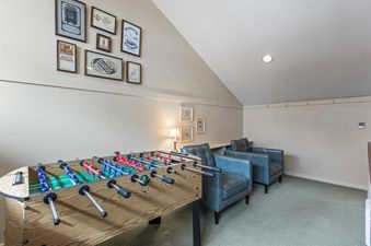 A game room at Snow Flower 127 featuring a foosball table, blue armchairs, and framed art on the walls.