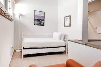 The bedroom of Snow Flower 152 Park City, featuring a white daybed with a trundle, a floor lamp, and wall art, offering a comfortable and serene retreat.