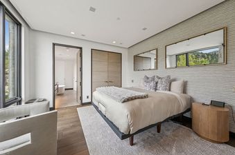 A modern bedroom with a large bed, two armchairs, and a view of the mountains from the window.