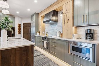 A modern rustic kitchen featuring sage green cabinets, marble countertops, stainless steel appliances, and natural wood accents.